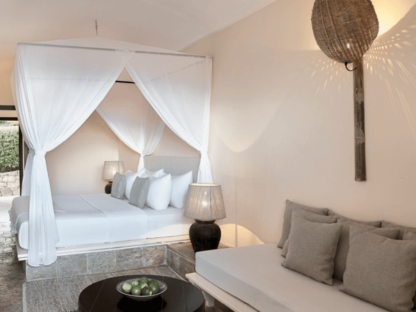 Interior of a Daphnila Bay Hideaway Bungalow with a four-poster bed, seating area, and ambient lighting, featuring a touch of luxury with a limited sea view.