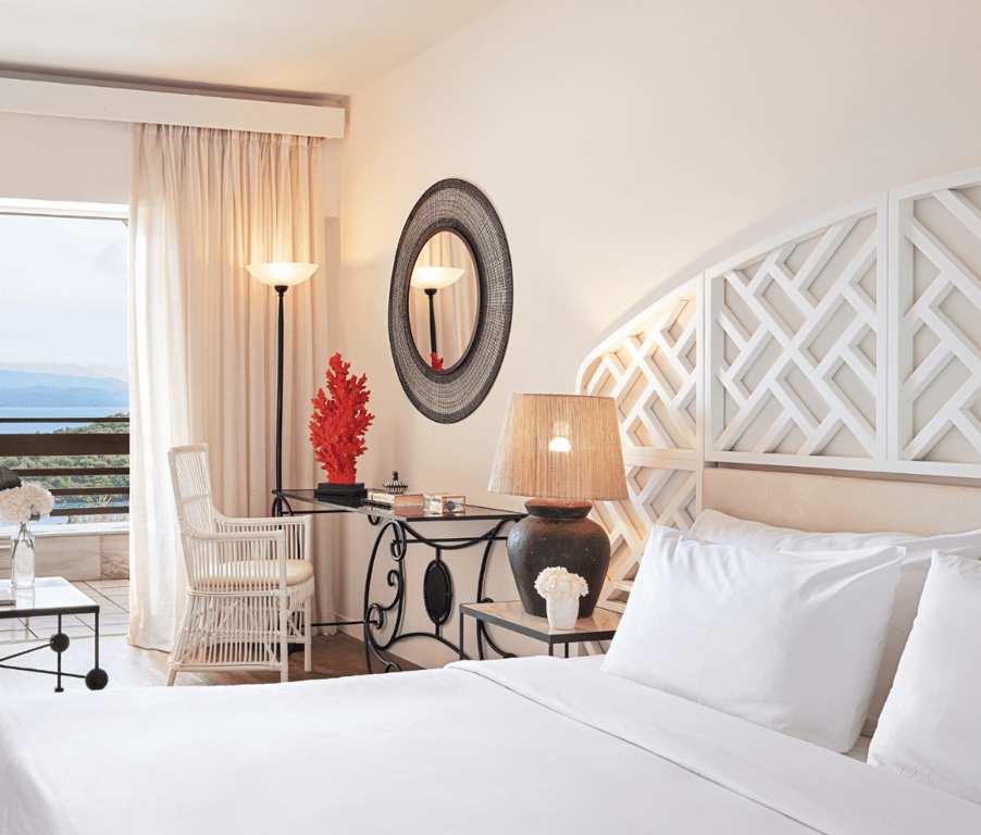 Elegantly decorated hotel room at Daphnila Bay Lux Me with white bed, lattice headboard, desk, and private balcony overlooking the sea.