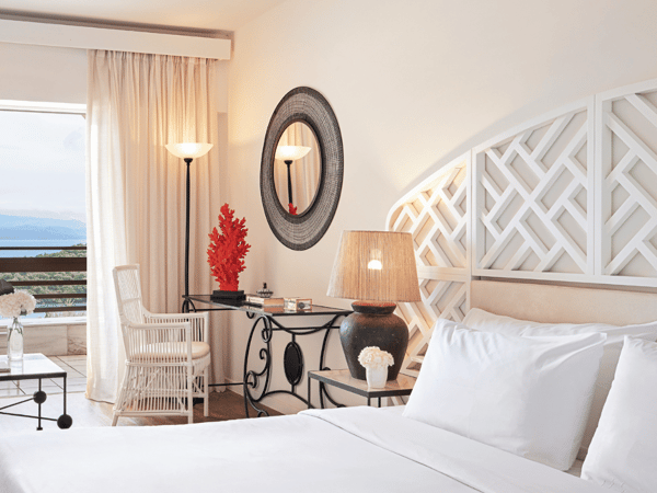 Elegantly decorated hotel room at Daphnila Bay Lux Me with white bed, lattice headboard, desk, and private balcony overlooking the sea.