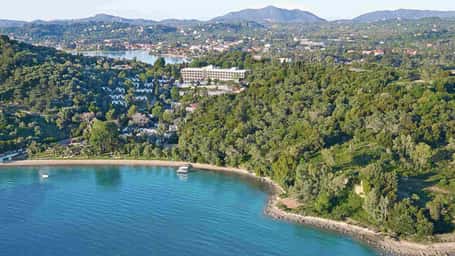 Aerial view of Daphnila Bay, Corfu, with green hills, sandy beach, and blue waters under a clear sky.