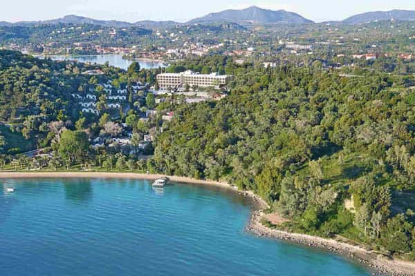 Aerial view of Daphnila Bay, Corfu, with green hills, sandy beach, and blue waters under a clear sky.