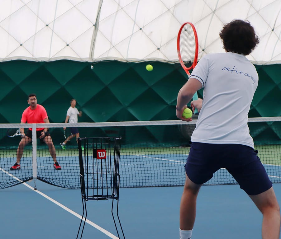 Tennis clinic at David Lloyd Northwood with two players engaged in an active rally on an indoor court under a dome.