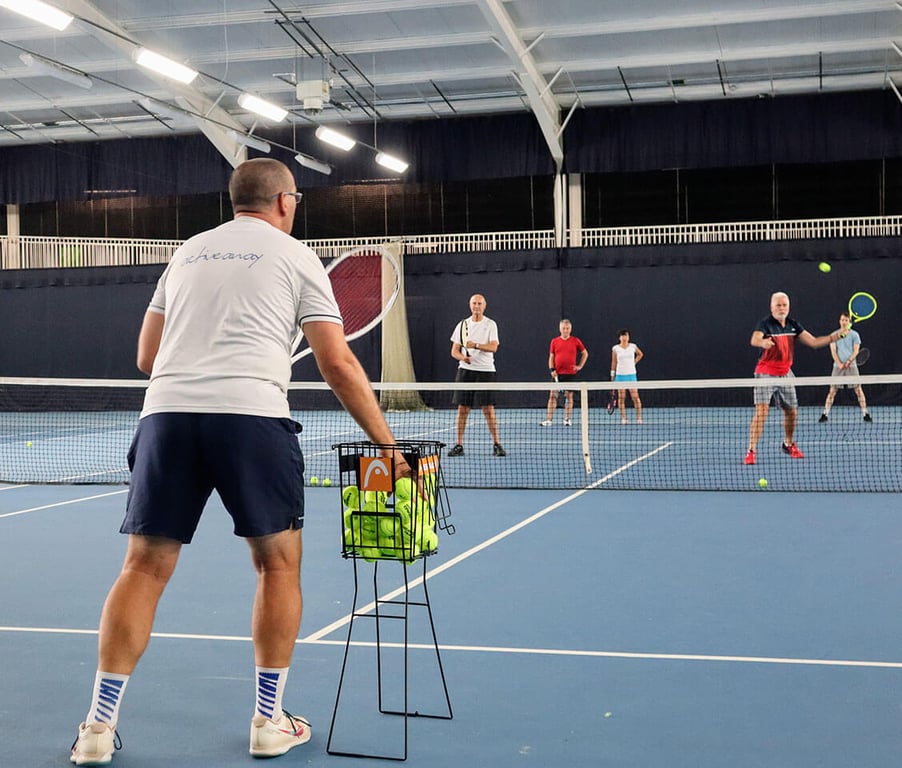 Group of tennis players in an indoor court at David Lloyd Southampton, with a coach instructing players near the net during a training drill.