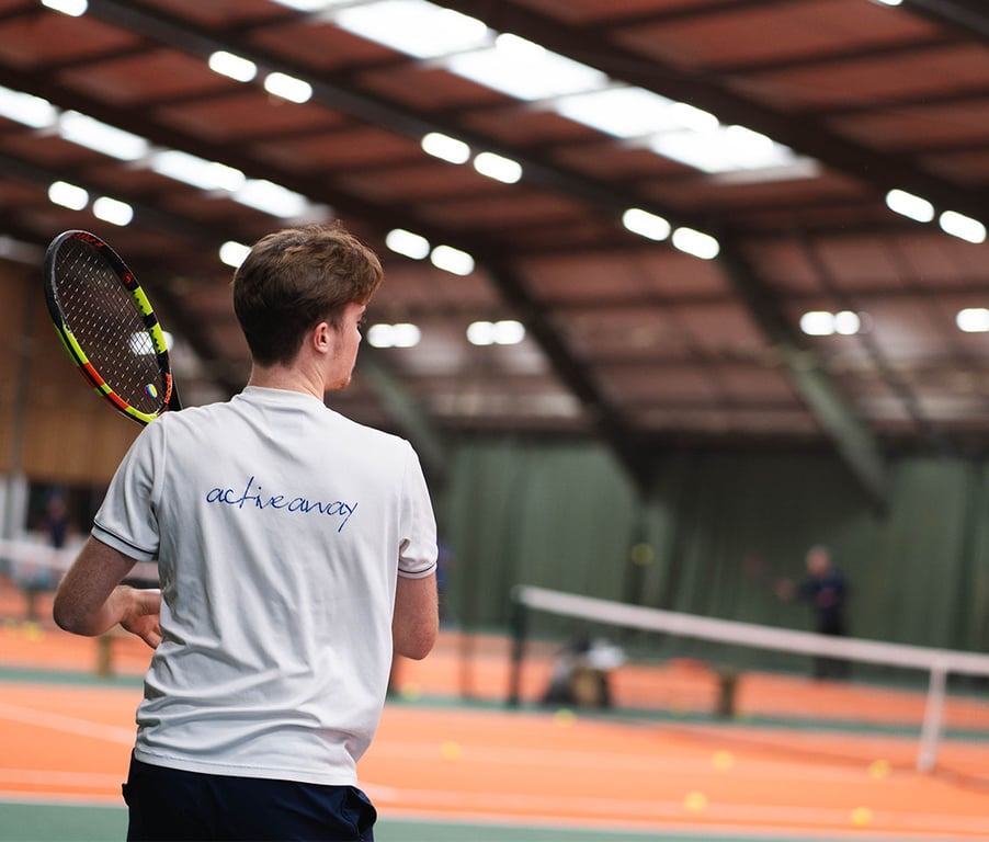 Tennis player in a clinic at David Lloyd West Bridgford's indoor tennis court, with tennis balls visible on the court.