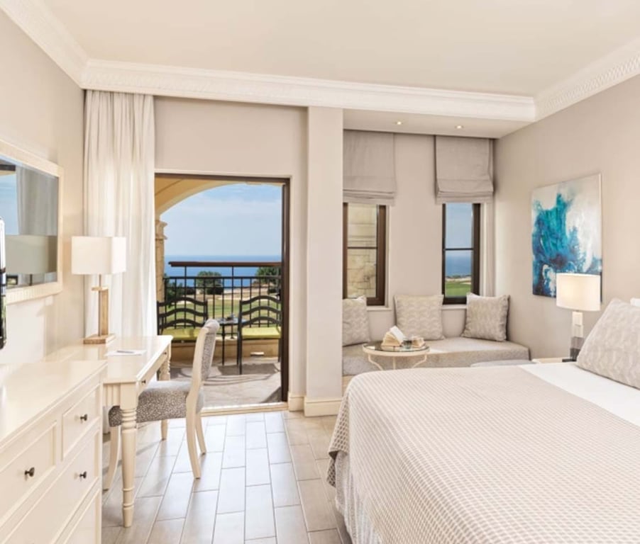 Deluxe Double Room with a double bed, seating area, and balcony offering views of a golf course and the sea.