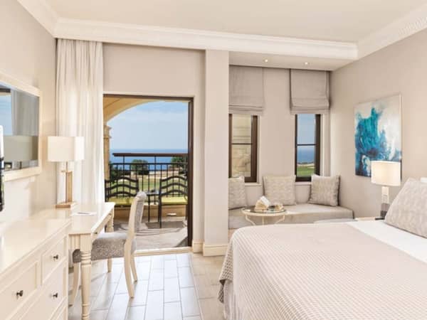 Deluxe Double Room with a double bed, seating area, and balcony offering views of a golf course and the sea.