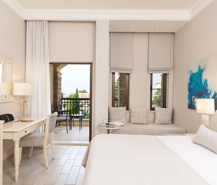 Deluxe double hotel room with neutral decor, a sitting area, and balcony overlooking a garden or pool.