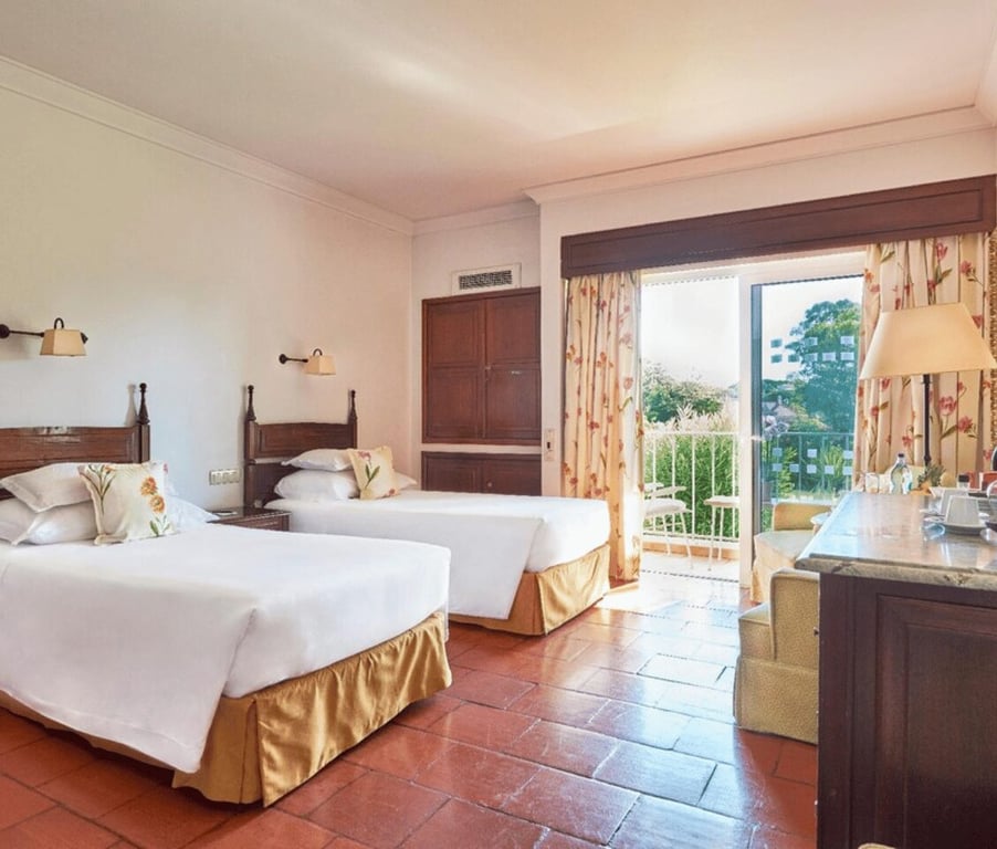 Dona Filipa Hotel Classic Room with two beds, white linens, wooden furniture, and a balcony overlooking greenery.