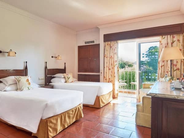 Dona Filipa Hotel Classic Room with two beds, white linens, wooden furniture, and a balcony overlooking greenery.