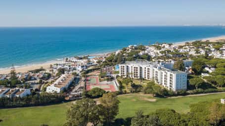 Aerial view of Dona Filipa resort in Algarve, featuring tennis courts, a golf course, and oceanic backdrop.
