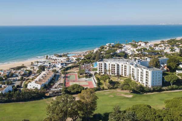 Aerial view of Dona Filipa resort in Algarve, featuring tennis courts, a golf course, and oceanic backdrop.
