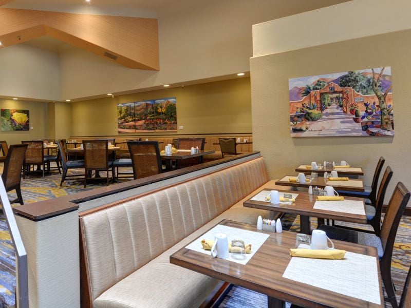 Dining area at El Conquistador Gallery featuring set tables with yellow napkins and wall art, creating a warm ambiance.