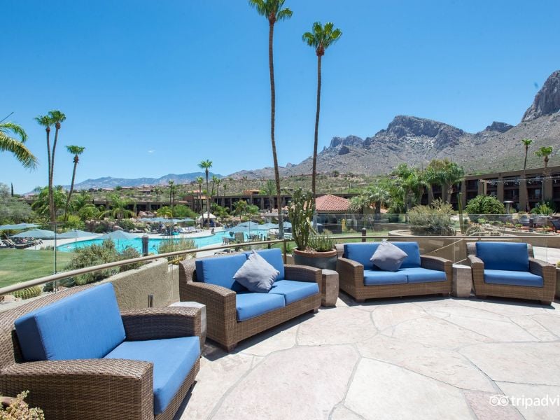Pool lounge area at El Conquistador Gallery with wicker furniture and blue cushions, surrounded by gardens and mountains.