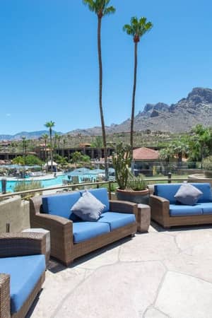 Pool lounge area at El Conquistador Gallery with wicker furniture and blue cushions, surrounded by gardens and mountains.