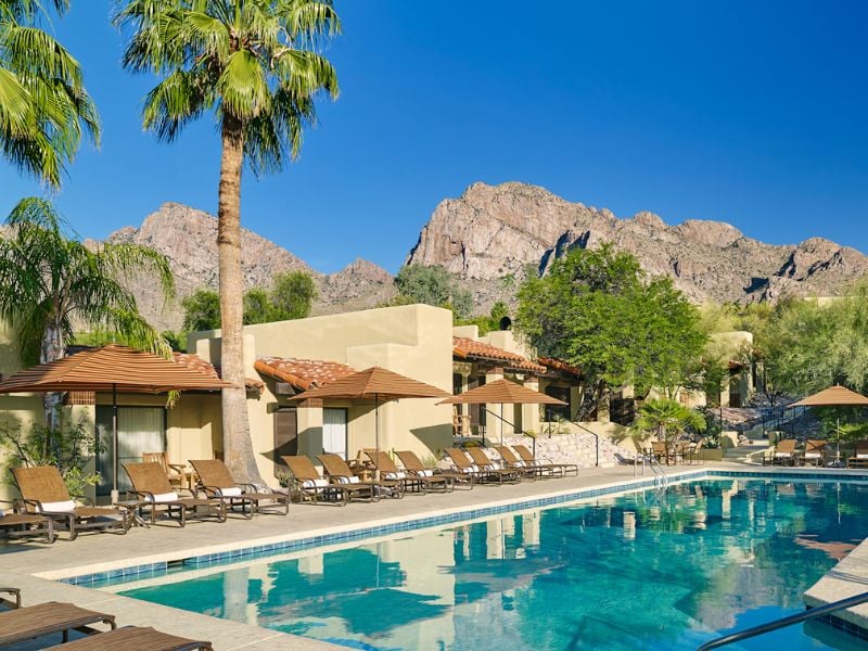 El Conquistador Resort pool area with sun loungers and parasols, set against a backdrop of mountains and clear skies.