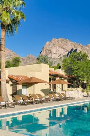 El Conquistador Resort pool area with sun loungers and parasols, set against a backdrop of mountains and clear skies.