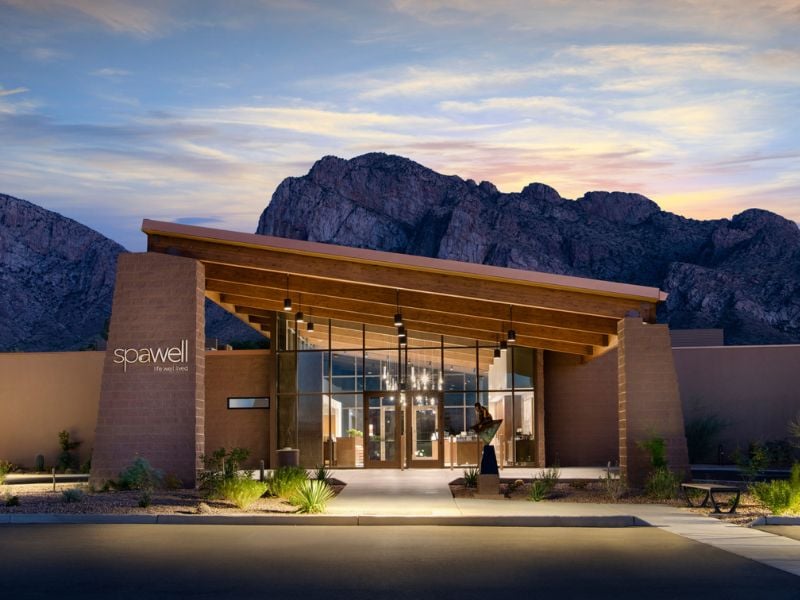 Exterior view of El Conquistador Gallery spa with mountains at sunset, highlighting modern architecture with glass and wood elements.