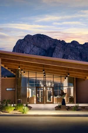 Exterior view of El Conquistador Gallery spa with mountains at sunset, highlighting modern architecture with glass and wood elements.
