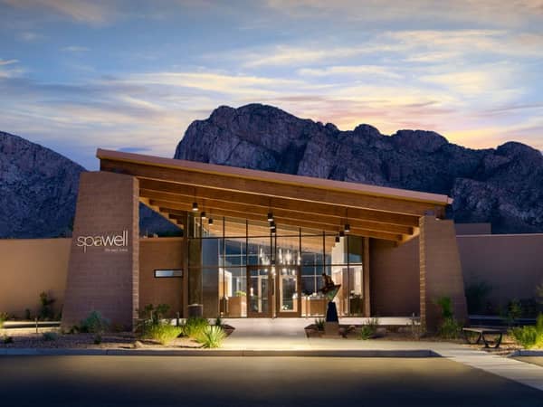 Exterior view of El Conquistador Gallery spa with mountains at sunset, highlighting modern architecture with glass and wood elements.