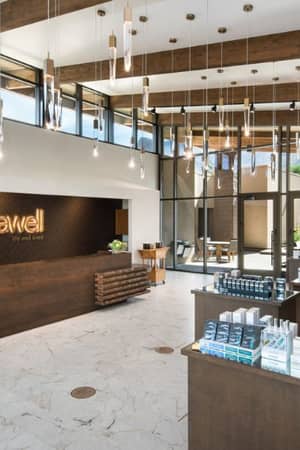 Luxurious spa interior at El Conquistador, featuring a wooden reception counter with 'spawell' logo, hanging lights, glass windows, and marble floors.