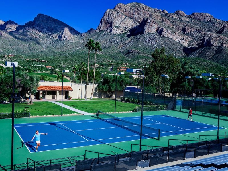 Tennis court at El Conquistador Gallery with players and mountain backdrop under a clear sky.