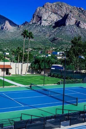 Tennis court at El Conquistador Gallery with players and mountain backdrop under a clear sky.