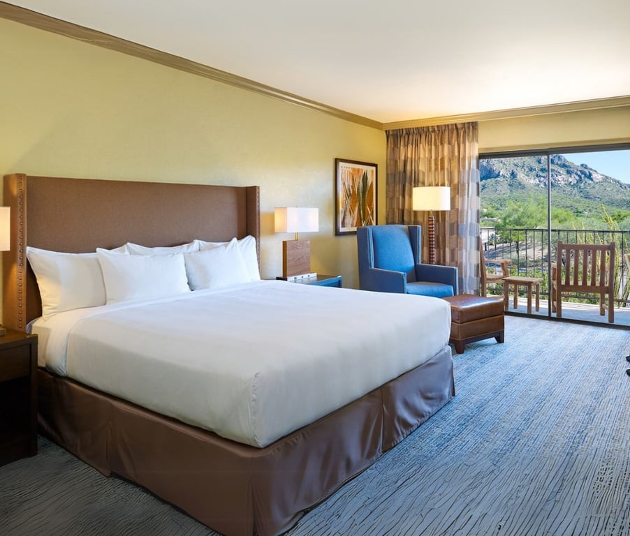 El Conquistador hotel room with a king bed, blue armchair, and a balcony offering mountain views.