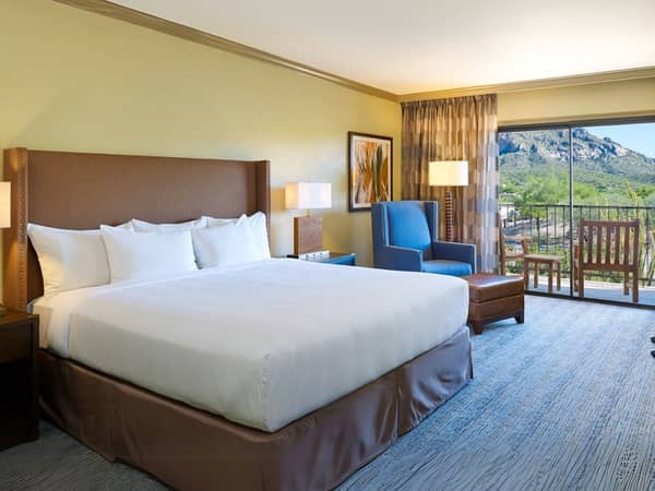El Conquistador hotel room with a king bed, blue armchair, and a balcony offering mountain views.