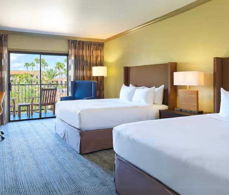 Hotel room at El Conquistador with two queen beds, a patio with outdoor seating, and a view of palm trees.