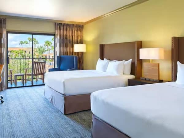 Hotel room at El Conquistador with two queen beds, a patio with outdoor seating, and a view of palm trees.
