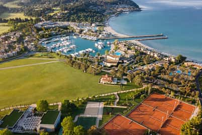Aerial view of Sani Beach resort in Greece, featuring tennis courts, a marina with yachts, and a beach along the Aegean Sea.