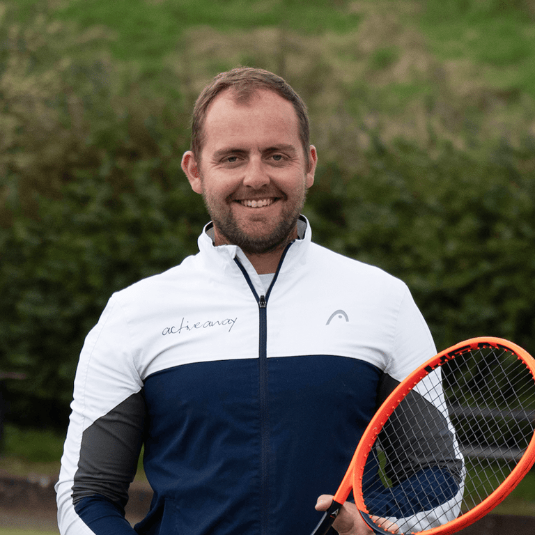 George Cann holding a tennis racquet, representing Active Away in sports attire, smiling outdoors.