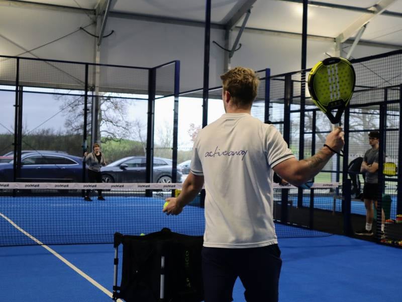 Tennis coaching session with a coach holding a padel tennis racket on a blue court at Gosling Sports Park.