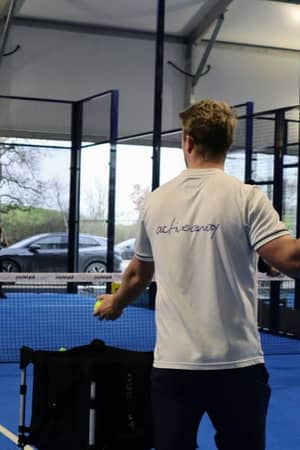 Tennis coaching session with a coach holding a padel tennis racket on a blue court at Gosling Sports Park.