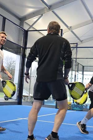 Three men playing padel tennis indoors at Great Western Golf, holding paddles on a blue court.