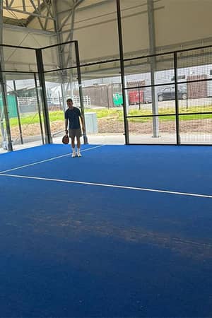 Two men playing padel tennis on a blue indoor court at Great Western Golf facility, with fencing and natural lighting.