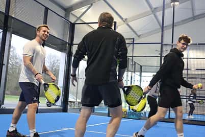 Three men participating in a padel clinic at Great Western Golf on a blue court, holding paddles and wearing sports gear.
