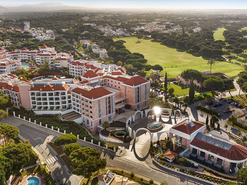 Aerial view of Hilton Vilamoura As Cascatas Golf Resort & Spa, surrounded by golf courses and greenery under a clear sky.