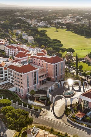 Aerial view of Hilton Vilamoura As Cascatas Golf Resort & Spa, surrounded by golf courses and greenery under a clear sky.