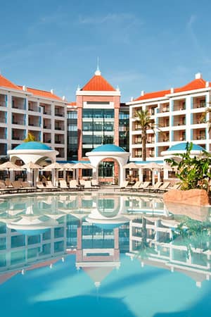 Exterior view of Hilton Vilamoura resort in Portugal, showcasing the central pool, sun loungers, tropical plants, and grand architectural design.