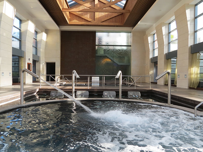 Indoor spa pool at Hilton Vilamoura with jets, wooden beams, and large windows letting in natural light.