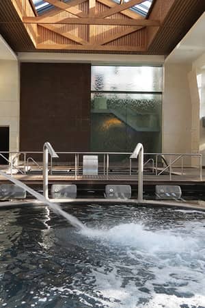 Indoor spa pool at Hilton Vilamoura with jets, wooden beams, and large windows letting in natural light.