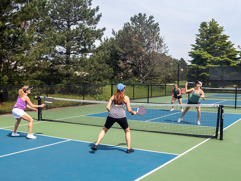 Women playing pickleball on an outdoor court at Hilton Vilamoura, surrounded by trees.