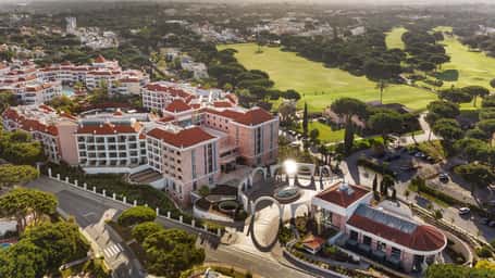 Aerial view of Hilton Vilamoura As Cascatas Golf Resort & Spa, with red-tiled roofs, greenery, and adjacent golf course in Vilamoura, Portugal.