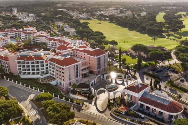 Aerial view of Hilton Vilamoura As Cascatas Golf Resort & Spa, with red-tiled roofs, greenery, and adjacent golf course in Vilamoura, Portugal.