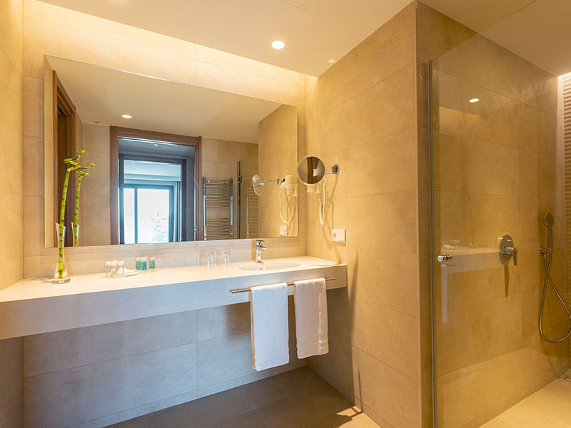 Modern bathroom at Hipotels Barrosa Park with wide vanity, illuminated mirror, sink with toiletries, and a spacious shower area.