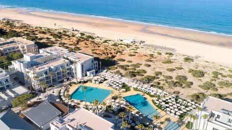 Aerial view of Hipotels Barrosa Park hotel with villas, a pool area, and beach access with sun loungers along the shore.