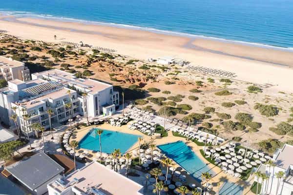 Aerial view of Hipotels Barrosa Park hotel with villas, a pool area, and beach access with sun loungers along the shore.