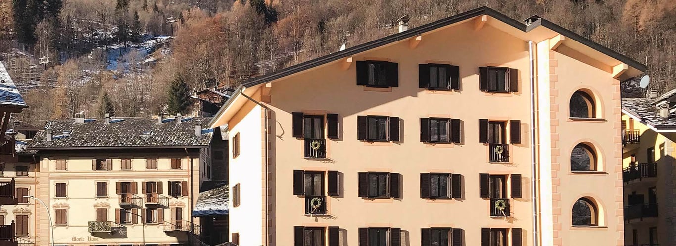 Exterior of Hotel Cristallo with beige facade and dark brown shutters, set against a mountainous backdrop.