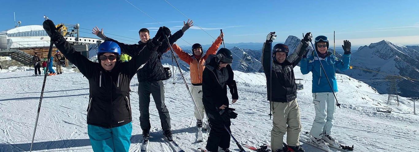 Group of skiers cheerfully posing on a snowy mountain slope near Hotel Cristallo under a clear sky.
